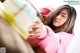 A woman in a pink sweatshirt is holding a stack of books.