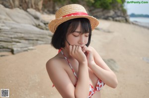 A woman in a straw hat sitting on a beach.