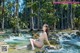 A woman in a white bikini sitting on a rock in a river.