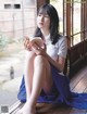 A woman sitting on a window sill reading a book.