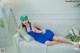 A woman in a blue dress and green hat laying on a white couch.