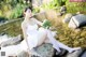 A woman in a white dress sitting on a rock by the water.